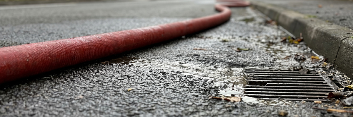 Fire hose on wet pavement with runoff flowing toward a storm drain