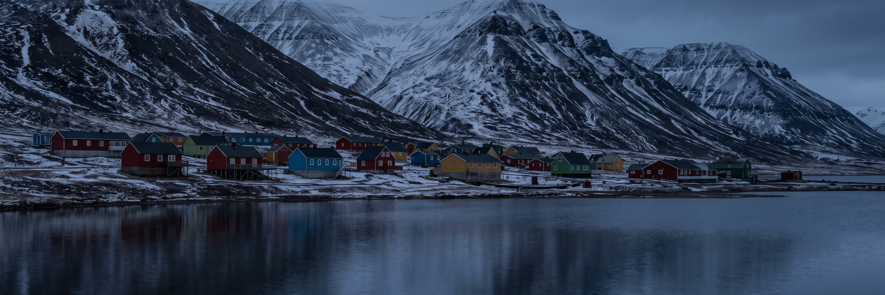 Colorful wooden houses below snow-streaked mountains beside a still Arctic lake